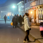 Menschen in warmer Kleidung, mit Lampions und Lichtern, laufen am frühen Abend durch eine Altstadt-Straße.