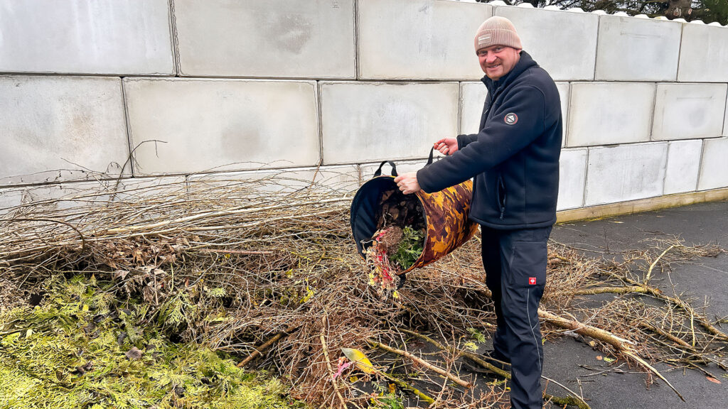 Ein Mann schüttet Grünabfälle aus einem Sack auf den Boden der Annahmestelle.