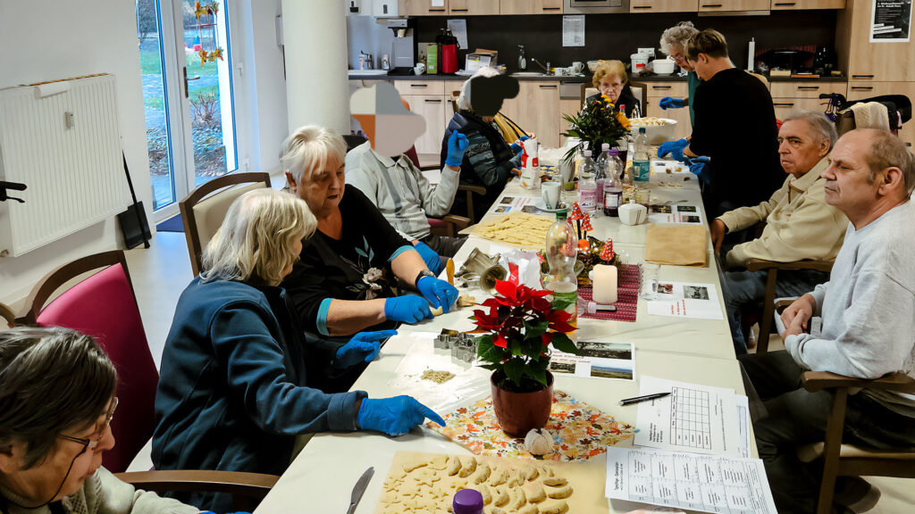 Ältere Menschen sitzen um einen weihnachtlich geschmückten Tisch und backen Plätzchen.