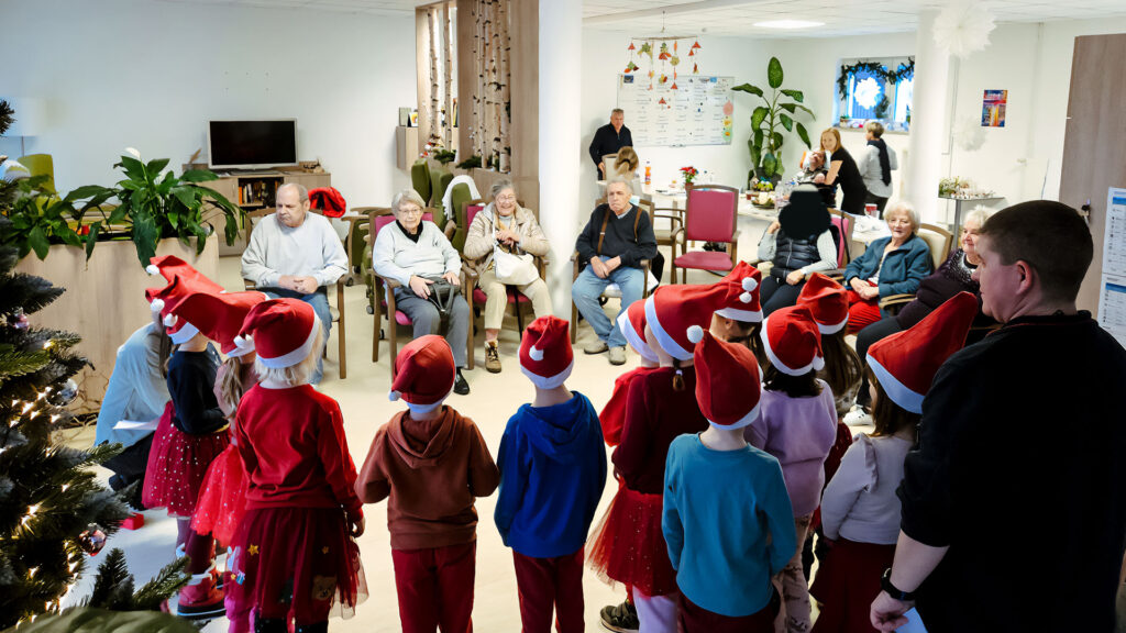 Kindergartenkinder mit ihren Erzieherinnen singen ein Ständchen für ältere Leute in weihnachtlicher Stimmung.