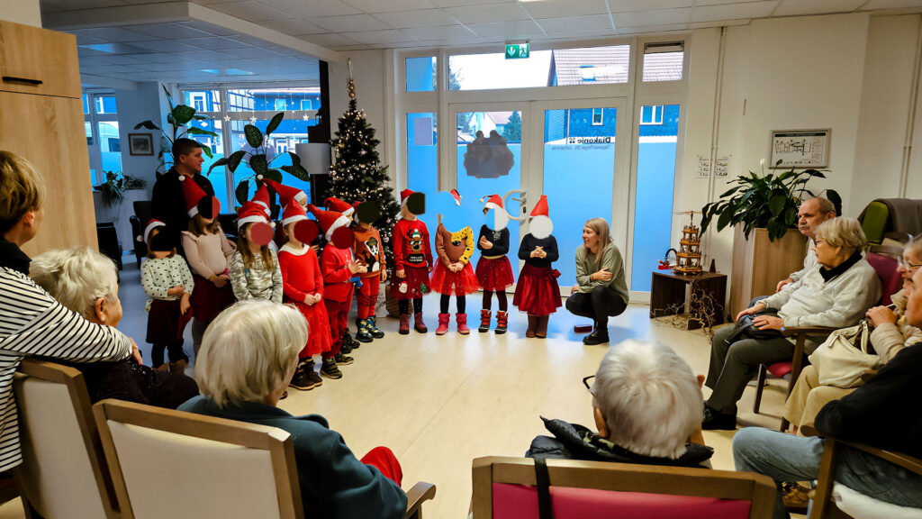 Kindergartenkinder mit ihren Erzieherinnen singen ein Ständchen für ältere Leute in weihnachtlicher Stimmung.