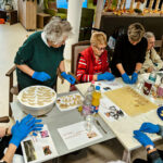 Ältere Menschen sitzen um einen weihnachtlich geschmückten Tisch und backen Plätzchen