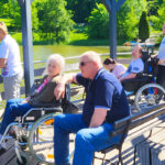 Bewohner und Pfleger, Männer und Frauen, der Diakonie Tagespflege an einem Teich auf einem hölzernen Aussichtsdeck