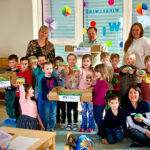 Kinder einer Kindergartengruppe und mehrere Erwachsene posieren für ein Foto mit grünen Pfannkuchen, man sieht Werbung für die Nordthüringer Volksbank.