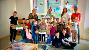 Kinder einer Kindergartengruppe und mehrere Erwachsene posieren für ein Foto mit grünen Pfannkuchen, man sieht Werbung für die Nordthüringer Volksbank.