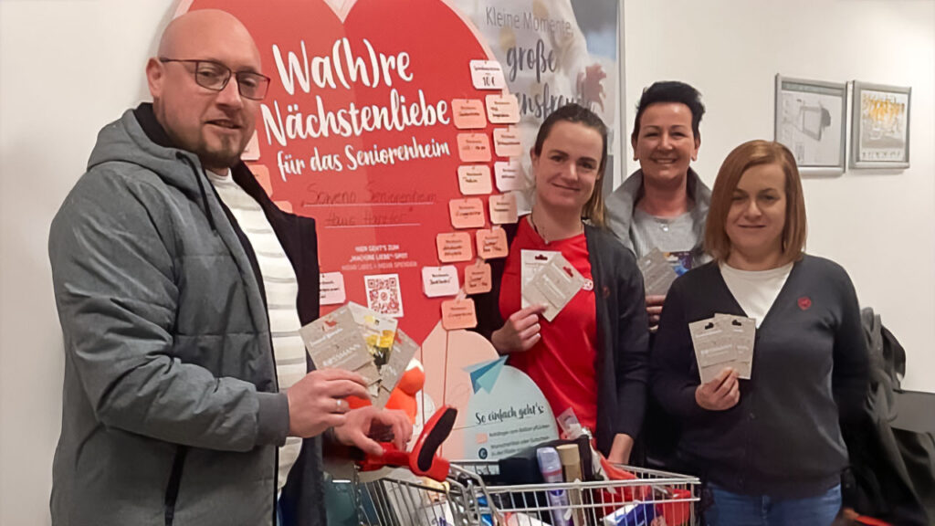 **ALT-Text:** Vier Personen posieren vor einem Plakat mit der Aufschrift "Wa(h)re Nächstenliebe für das Seniorenheim". Sie halten Wunschzettel in den Händen und stehen neben einem Einkaufswagen voller Spenden. Das Bild zeigt die erfolgreiche Teilnahme an einer ROSSMANN-Spendenkampagne für das Haus Harztor.